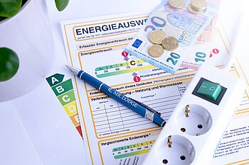 Zu sehen ist ein Energieausweis, eine Mehrfachsteckdose, und Geld.