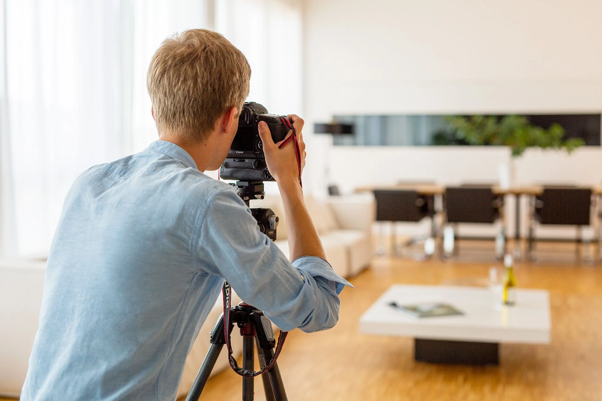 Immobilienfotograf nimmt mit Stativ und Kamera ein Wohnzimmer auf